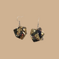 Pair of black and gold geometric origami earrings with a floral pattern on a beige background.