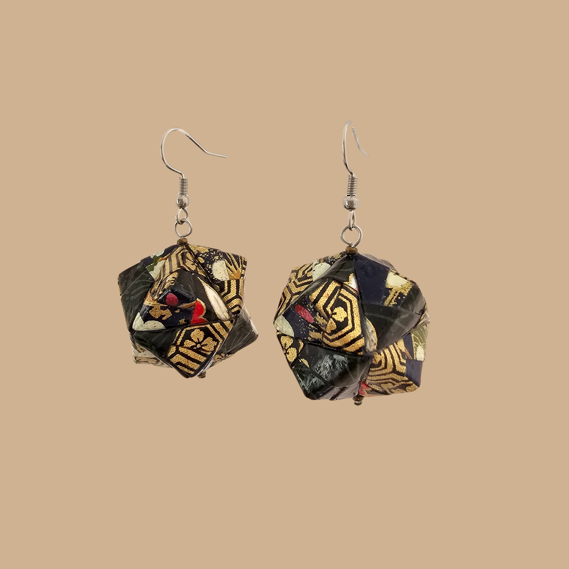 Pair of black and gold geometric origami earrings with a floral pattern on a beige background.