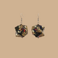 Pair of black and gold geometric origami earrings with a floral pattern on a beige background.
