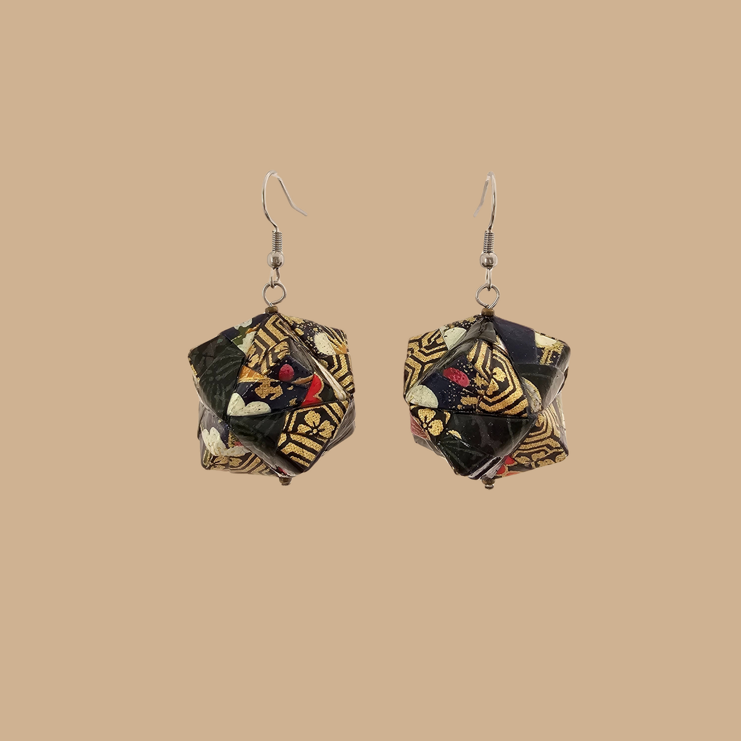 Pair of black and gold geometric origami earrings with a floral pattern on a beige background.
