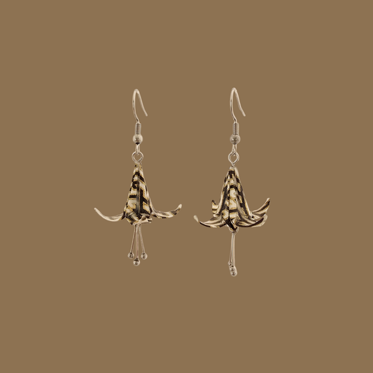 Black and gold origami lily earrings with a floral and geometric pattern on a beige background
