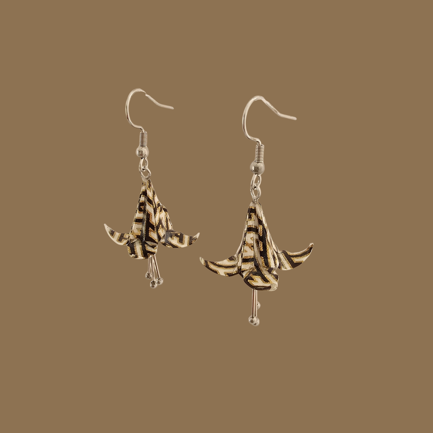 Black and gold origami lily earrings with a floral and geometric pattern on a beige background