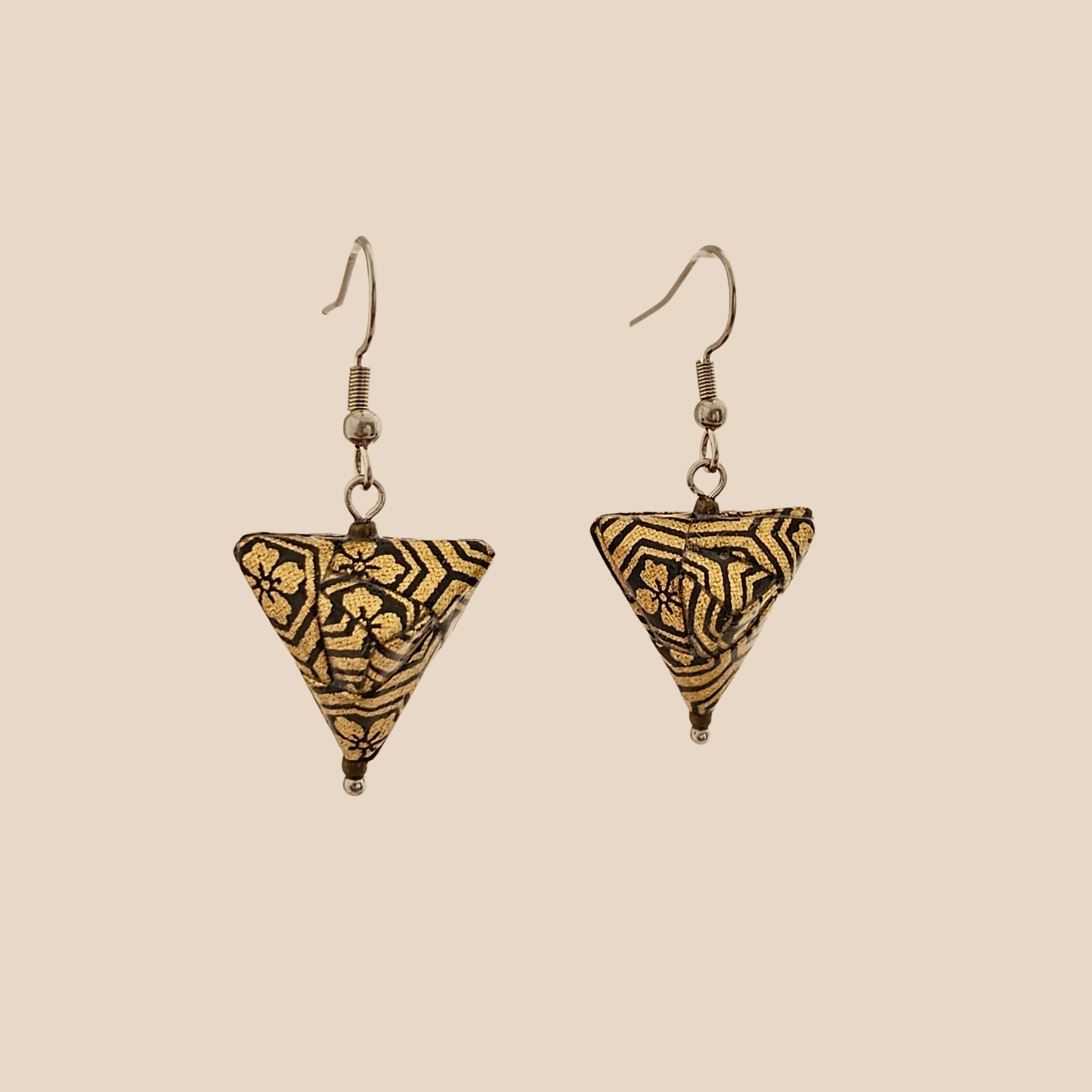 Black and Gold triangle geometric origami earrings with a floral and geometric pattern on a beige background