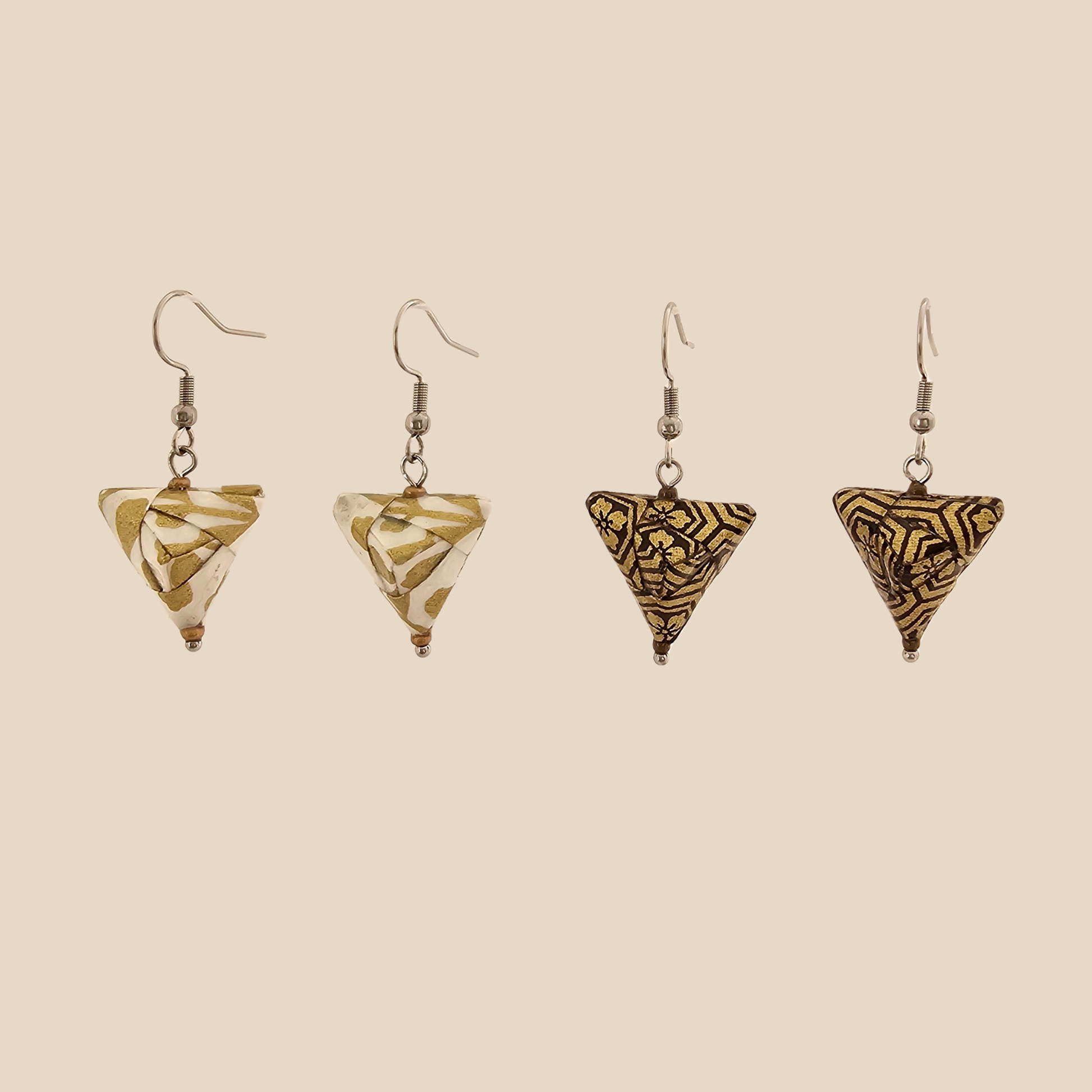 Two paris of white, gold and black triangle geometric origami earrings with a floral and geometric pattern on a beige background