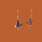 A pair of blue, purple, orange origami lily earrings with a floral and geometric pattern on an orange background