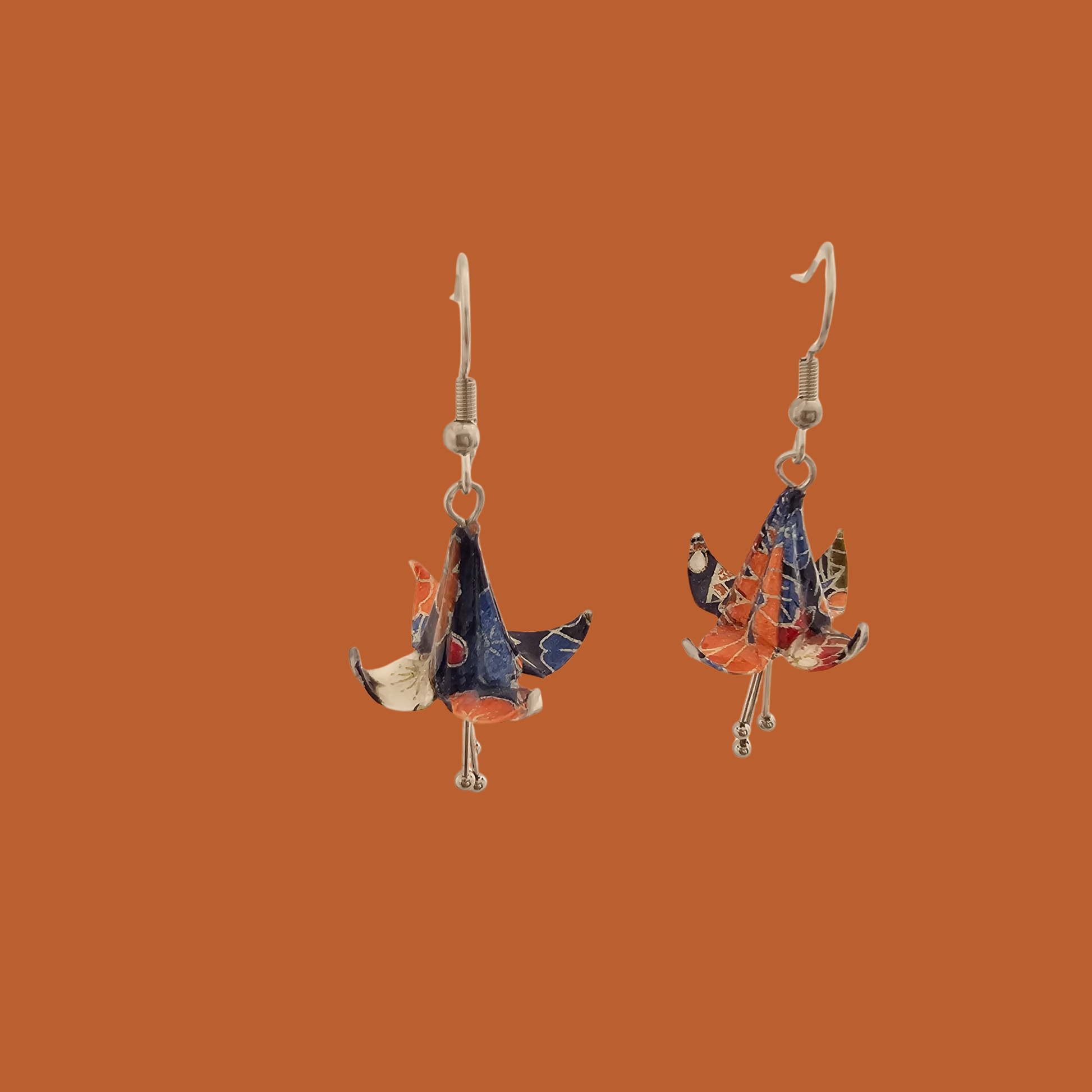 A pair of blue, purple, orange origami lily earrings with a floral and geometric pattern on an orange background