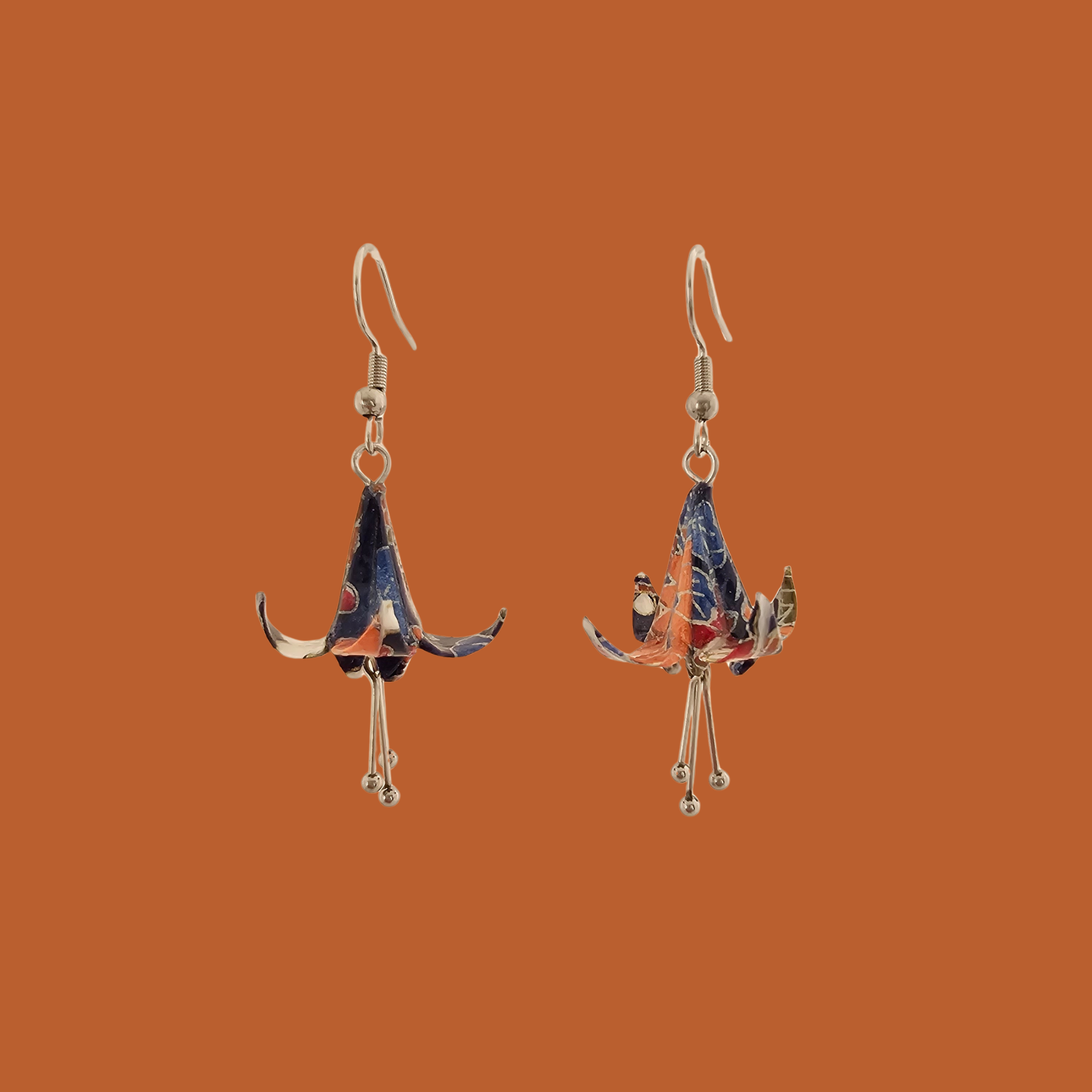 A pair of blue, purple, orange origami lily earrings with a floral and geometric pattern on an orange background