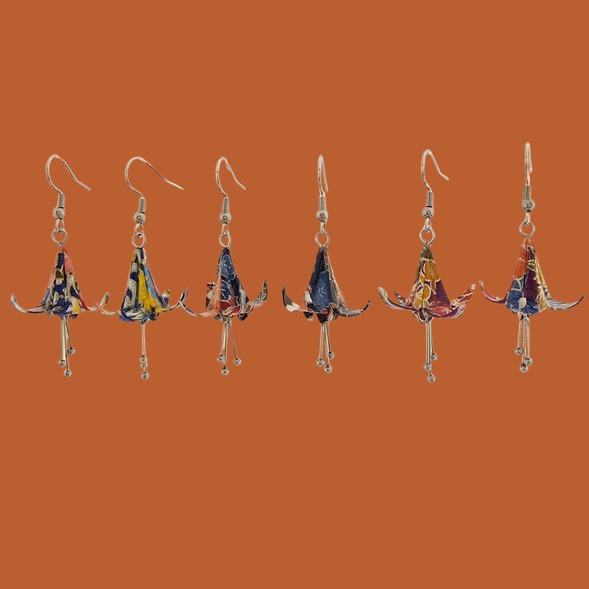 A pair of blue, purple, orange origami lily earrings with a floral and geometric pattern on an orange background