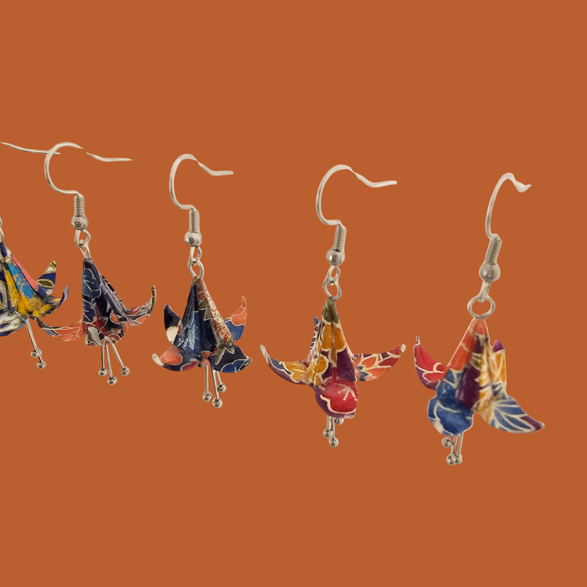 A pair of blue, purple, orange origami lily earrings with a floral and geometric pattern on an orange background
