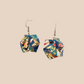 Pair of blue, white, and pink geometric origami earrings with a floral pattern on a beige background.