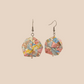 Pair of blue and pink geometric origami earrings with a floral pattern on a beige background.