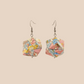 Pair of black and gold geometric origami earrings with a floral pattern on a beige background.