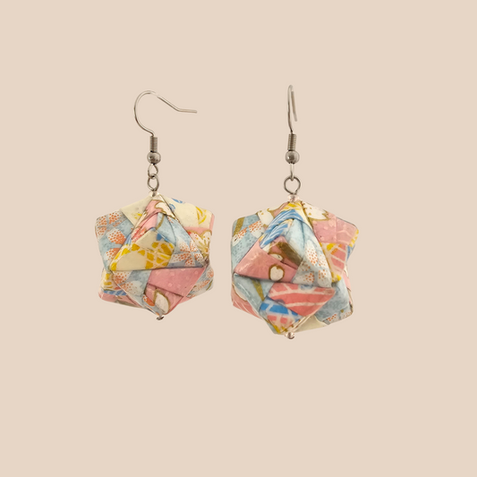 Pair of black and gold geometric origami earrings with a floral pattern on a beige background.