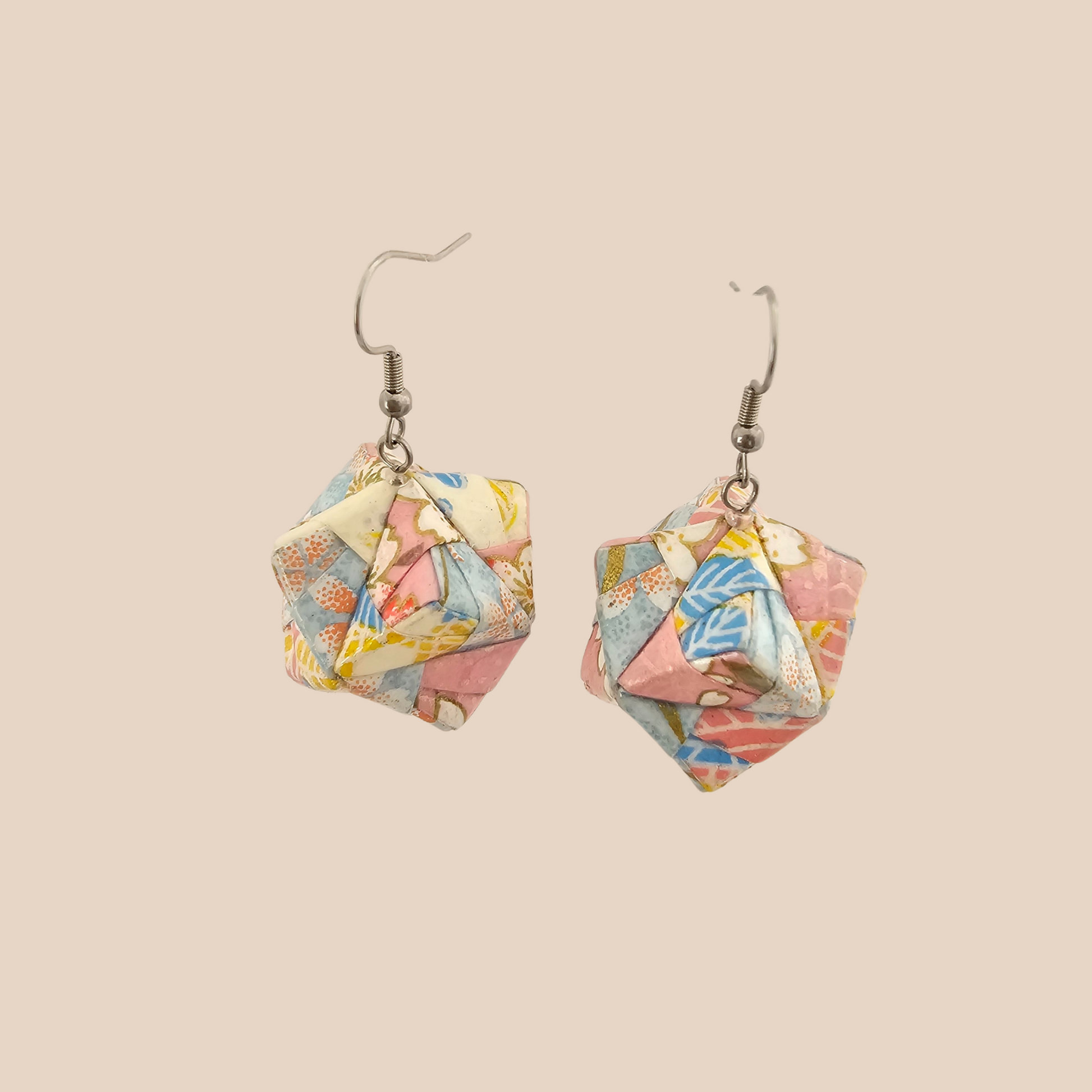 Pair of black and gold geometric origami earrings with a floral pattern on a beige background.