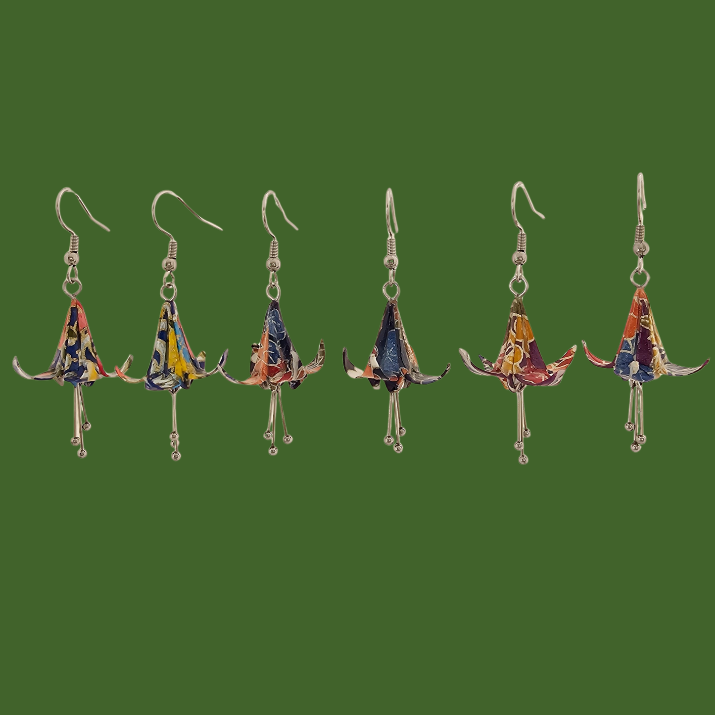 Three pairs of blue and purple origami lily earrings with a floral and geometric pattern on a beige background