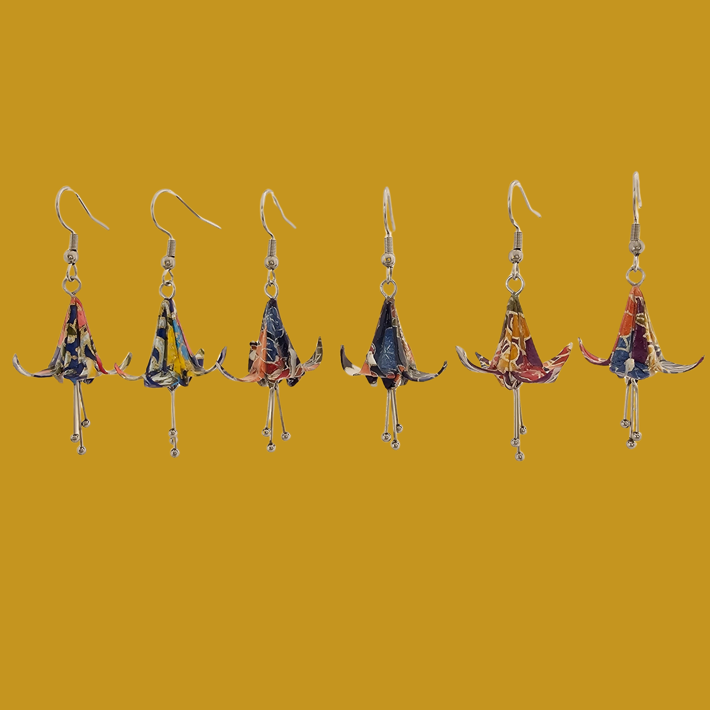 A pair of blue origami lily earrings with a floral and geometric pattern on a yellow background