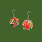 Pair of pink and green geometric origami earrings with a floral pattern on a green background.