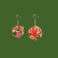 Pair of pink and green geometric origami earrings with a floral pattern on a green background.