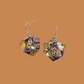 Pair of purple and gold geometric origami earrings with a floral pattern on a beige background.