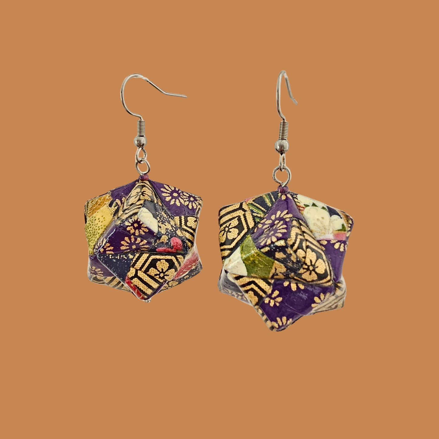 Pair of purple and gold geometric origami earrings with a floral pattern on a beige background.