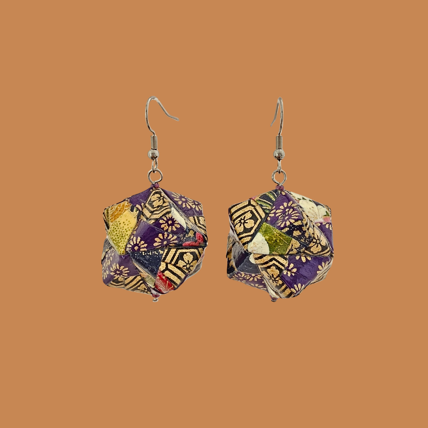 Pair of purple and gold geometric origami earrings with a floral pattern on a beige background.