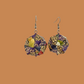 Pair of purple and gold geometric origami earrings with a floral pattern on a beige background.
