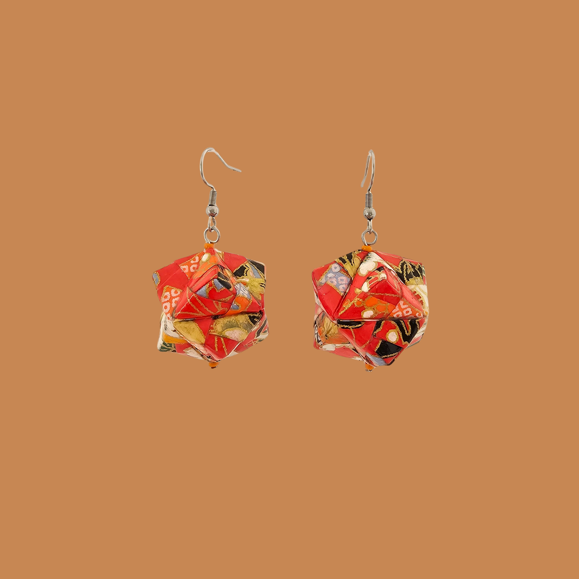 Pair of red, gold, and black geometric origami earrings with a floral pattern on a brown background