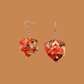 Pair of red, gold, and black geometric origami earrings with a floral pattern on a brown background