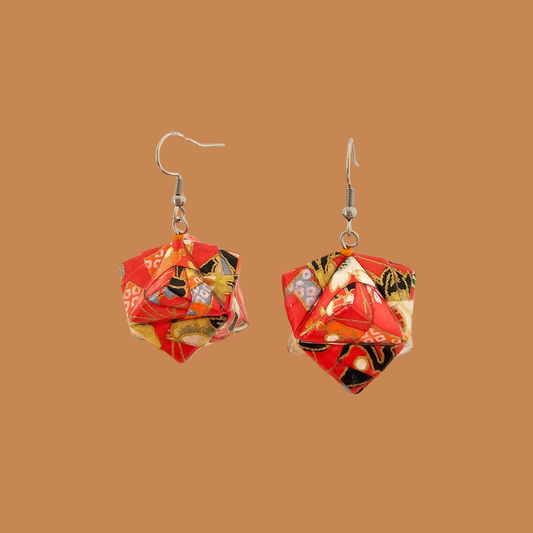 Pair of red, gold, and black geometric origami earrings with a floral pattern on a brown background