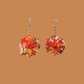 Pair of red, gold, and black geometric origami earrings with a floral pattern on a brown background