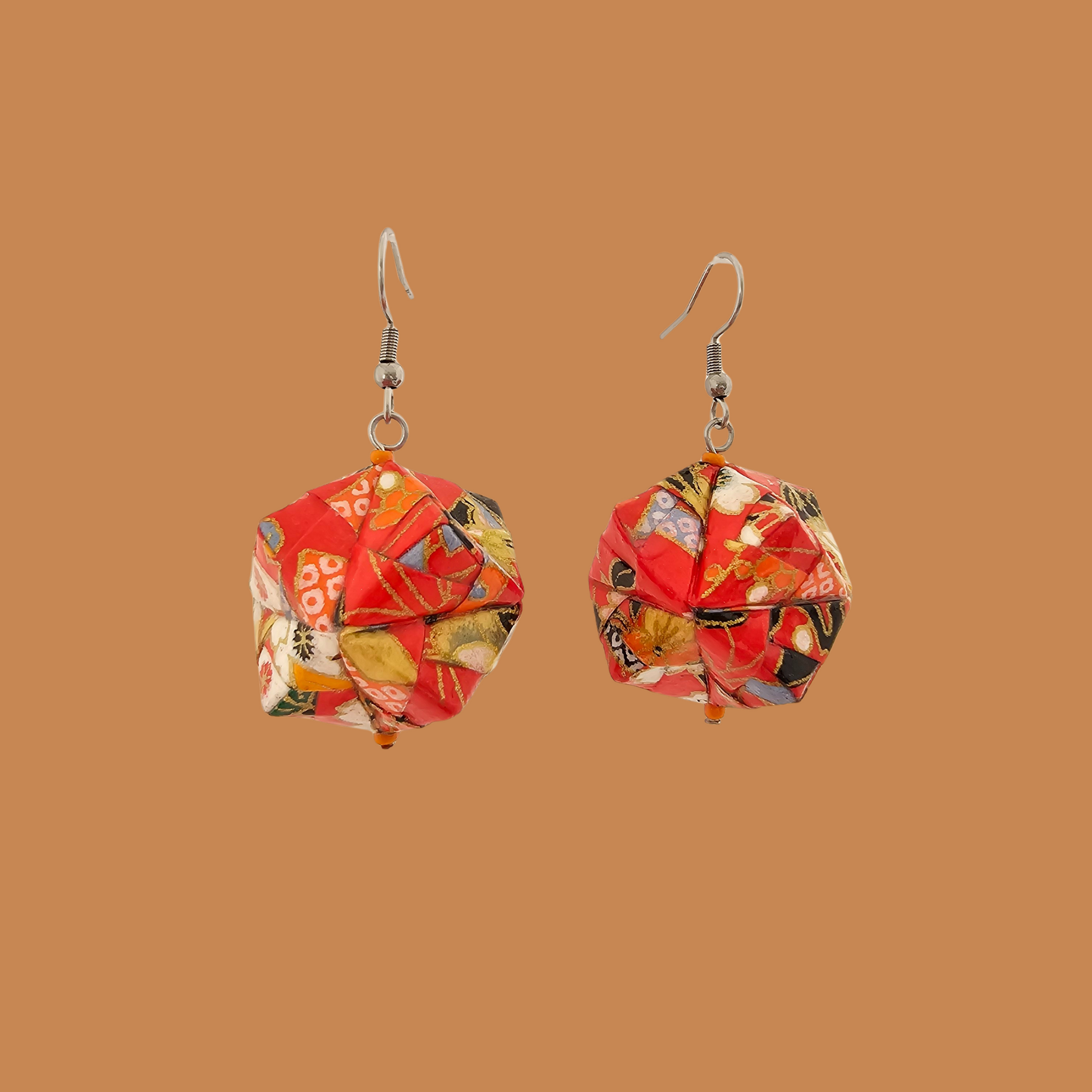 Pair of red, gold, and black geometric origami earrings with a floral pattern on a brown background