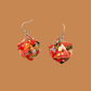 Pair of red, gold, and black geometric origami earrings with a floral pattern on a brown background