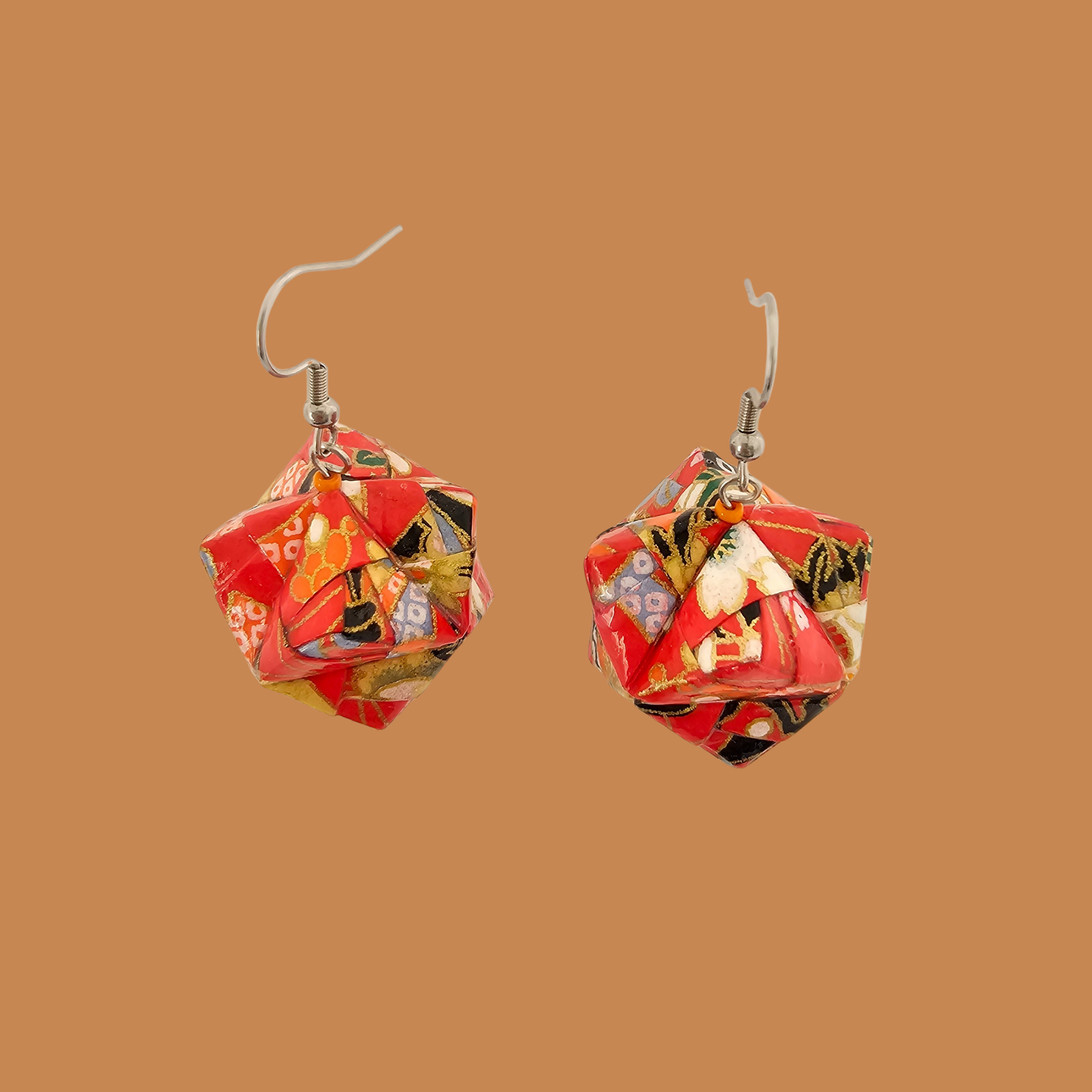Pair of red, gold, and black geometric origami earrings with a floral pattern on a brown background