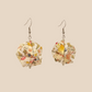 Pair of white geometric origami earrings with a floral pattern on a beige background