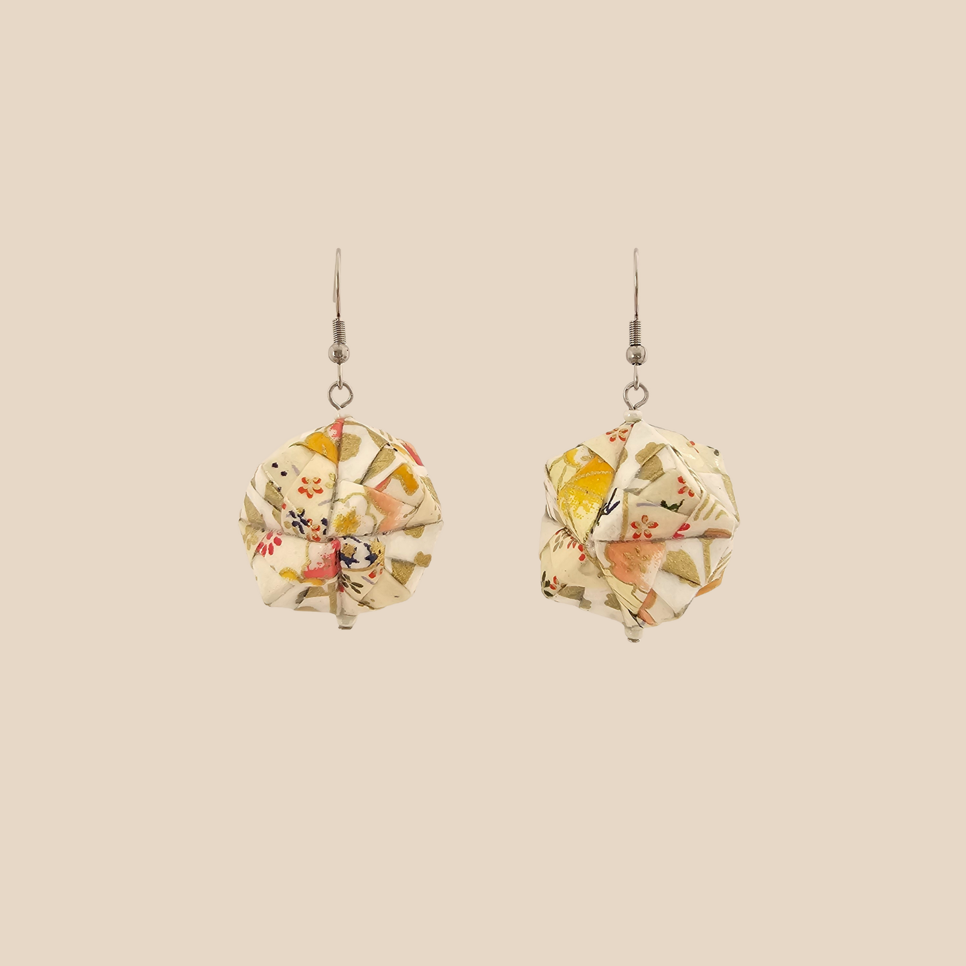 Pair of white geometric origami earrings with a floral pattern on a beige background