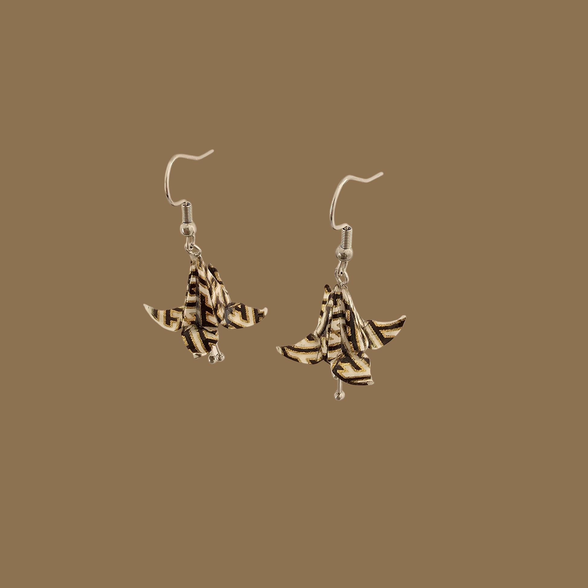 White, black and gold origami lily earrings with a floral and geometric pattern on a beige background