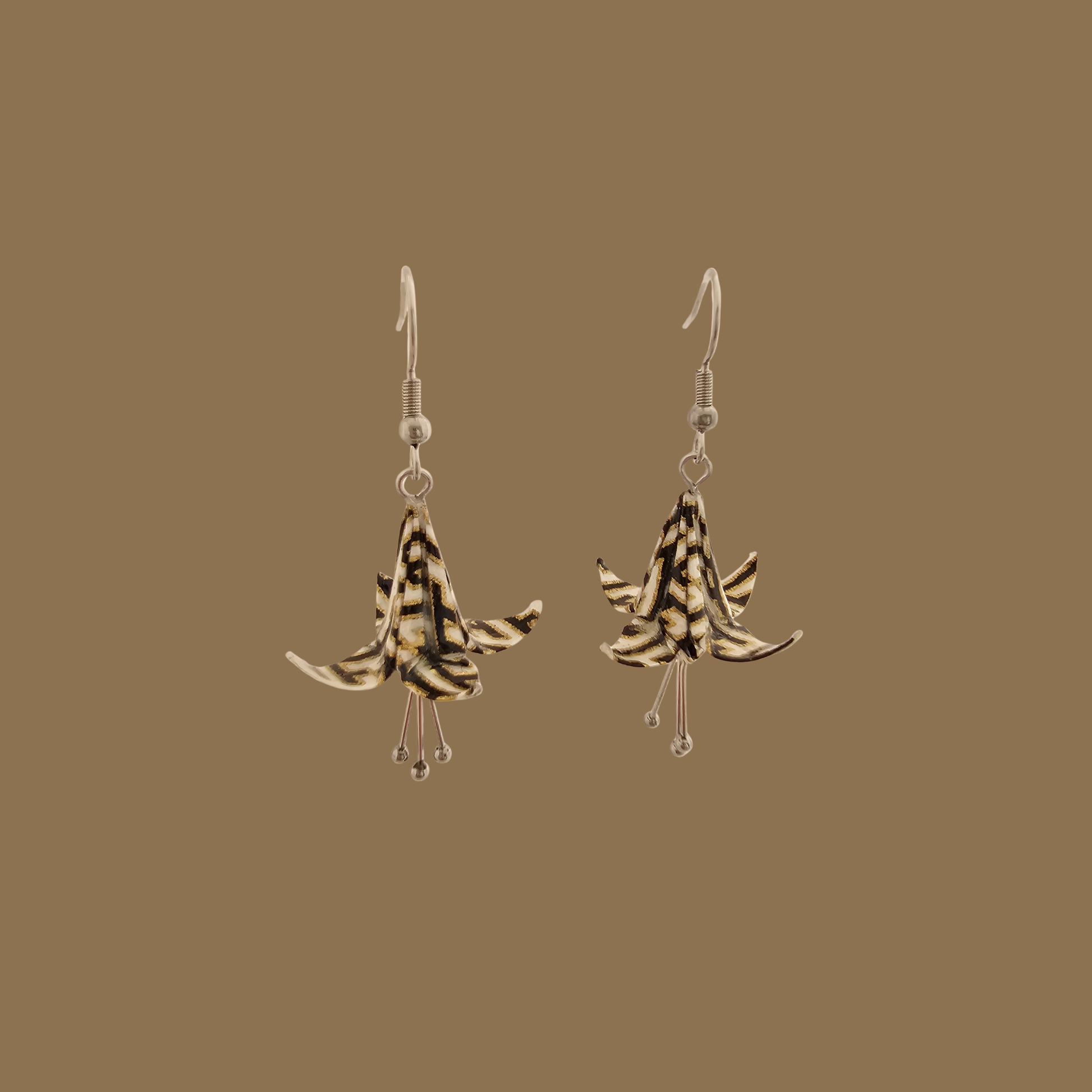 Black and gold origami lily earrings with a floral and geometric pattern on a beige background