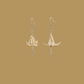 White and gold origami lily earrings with a floral and geometric pattern on a beige background