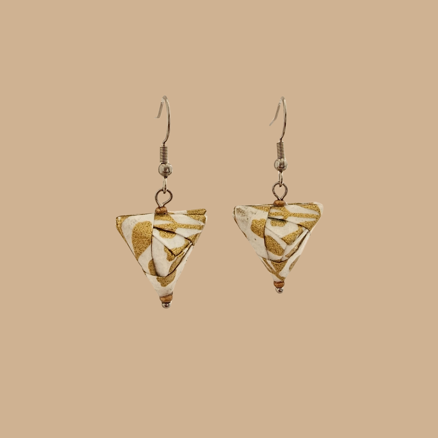 White and Gold triangle geometric origami earrings with a floral and geometric pattern on a beige background